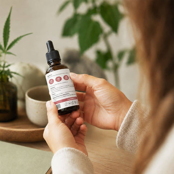 Frau, die das Etikett auf einer Formula Swiss Cannabinoid-Ölflasche in einer hellen Innenumgebung überprüft.